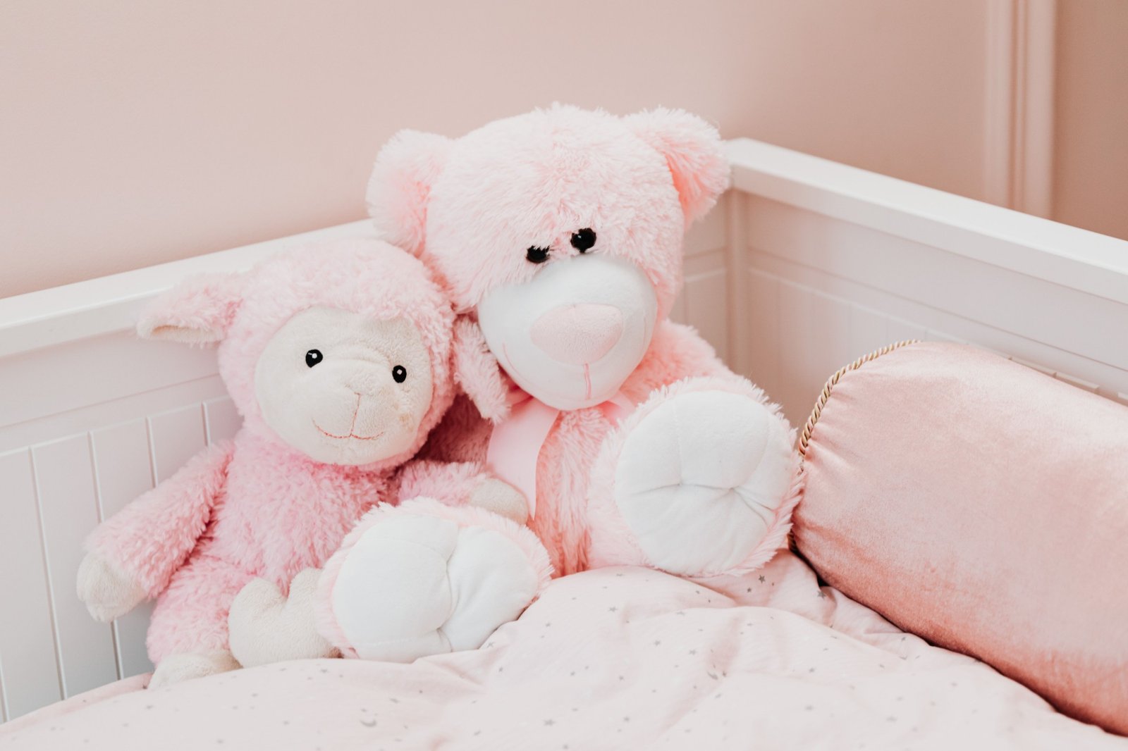 Deux peluches roses, un ourson et un agneau, dans un lit de bébé